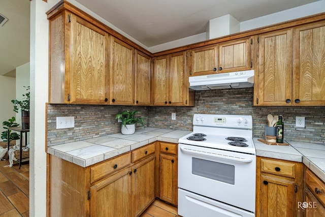 kitchen with brown cabinetry, white range with electric stovetop, under cabinet range hood, and tile countertops