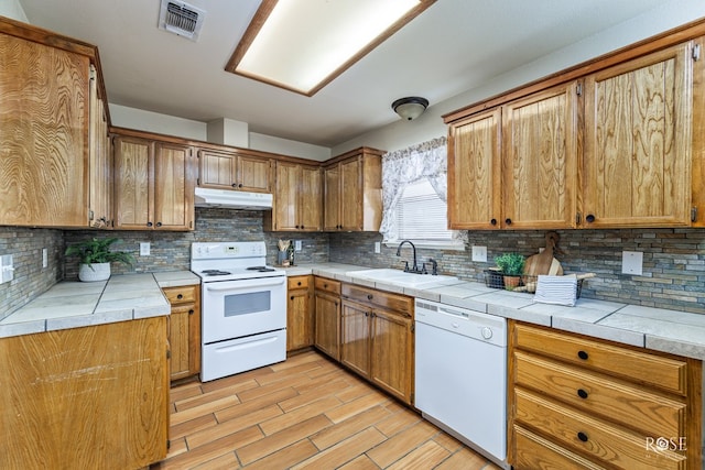 kitchen with white appliances, a sink, under cabinet range hood, and tile countertops