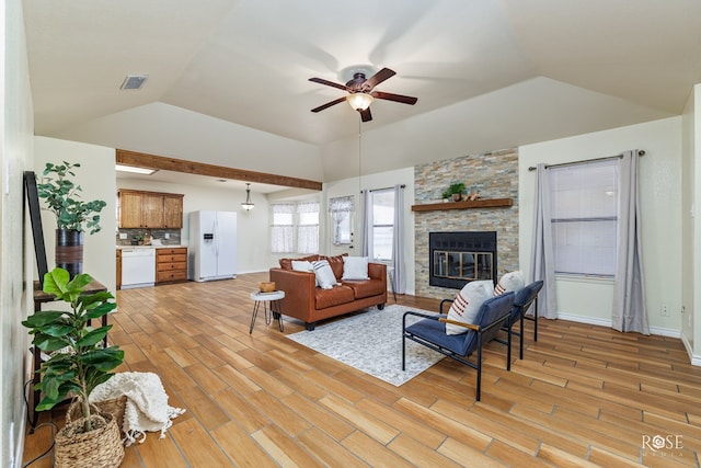 living room with light wood finished floors, visible vents, a ceiling fan, vaulted ceiling, and a stone fireplace