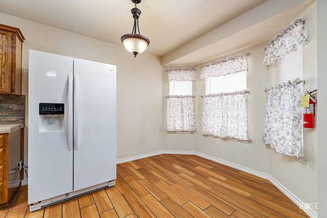 kitchen featuring baseboards, light countertops, white fridge with ice dispenser, light wood finished floors, and brown cabinetry