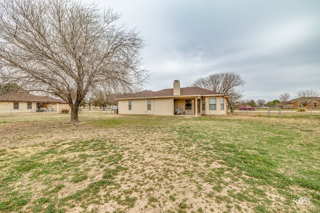 back of house with a chimney, fence, a lawn, and stucco siding