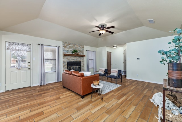 living room with visible vents, a ceiling fan, lofted ceiling, a stone fireplace, and light wood-type flooring