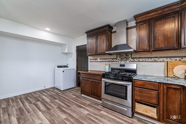 kitchen with dark brown cabinetry, wall chimney exhaust hood, washer / dryer, stainless steel range with gas stovetop, and decorative backsplash