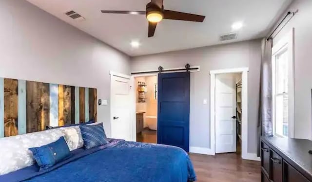 bedroom with a barn door, baseboards, visible vents, and dark wood-style floors