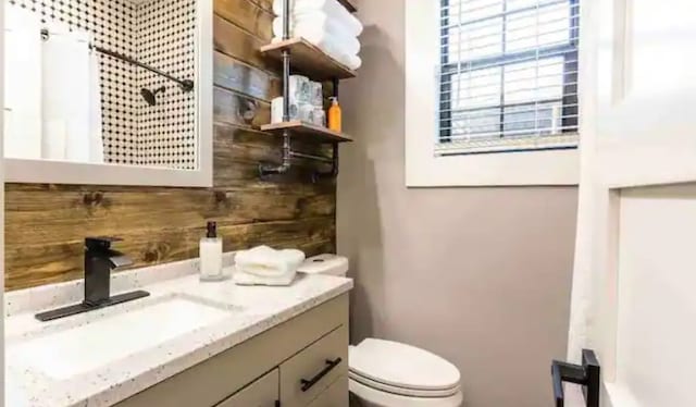 full bathroom featuring a shower with curtain, wooden walls, toilet, and vanity