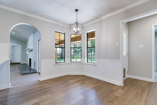 unfurnished dining area featuring lofted ceiling, hardwood / wood-style floors, crown molding, and a notable chandelier