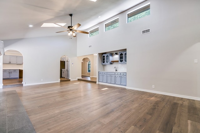 unfurnished living room with ceiling fan, sink, hardwood / wood-style floors, and a high ceiling