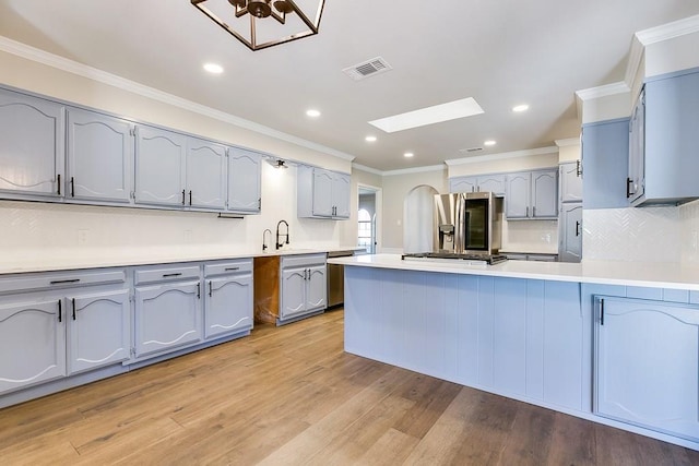 kitchen with a skylight, tasteful backsplash, ornamental molding, stainless steel appliances, and light wood-type flooring