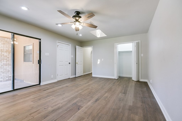 unfurnished bedroom featuring ceiling fan, access to exterior, a skylight, and light hardwood / wood-style floors