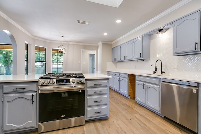 kitchen featuring sink, tasteful backsplash, hanging light fixtures, light wood-type flooring, and stainless steel appliances