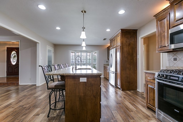 kitchen with appliances with stainless steel finishes, a breakfast bar, sink, dark hardwood / wood-style flooring, and a kitchen island with sink