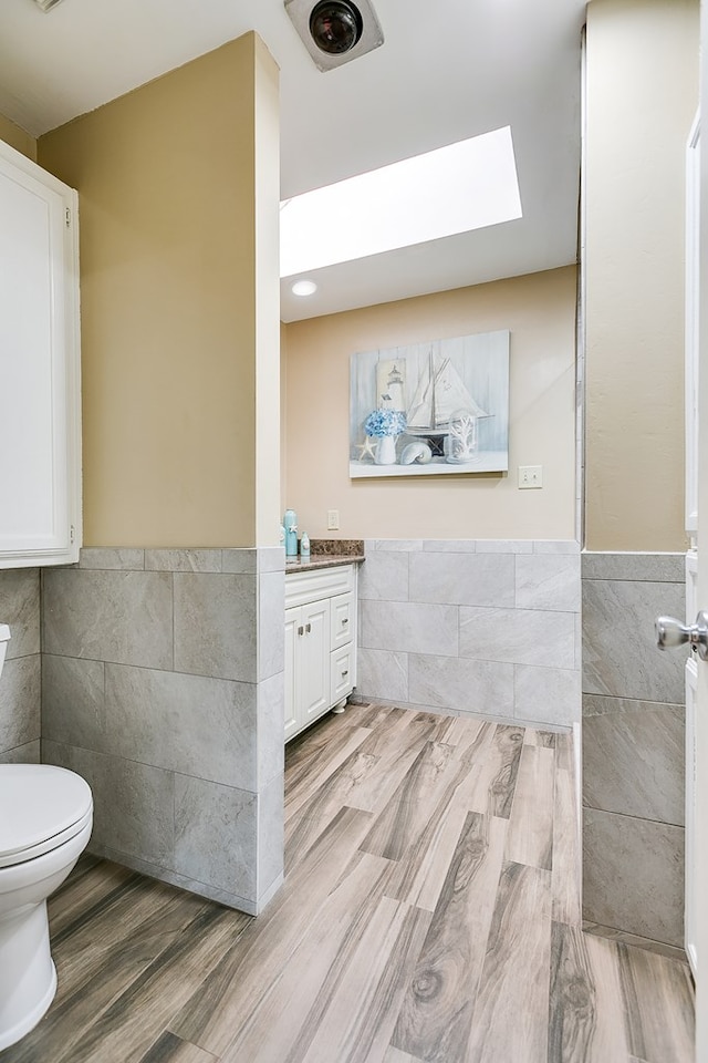 bathroom with a skylight, vanity, tile walls, and toilet