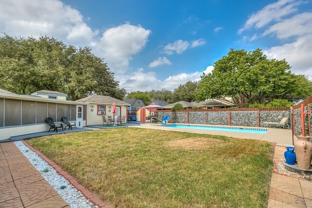 view of yard featuring a fenced in pool, a sunroom, an outbuilding, and a patio area