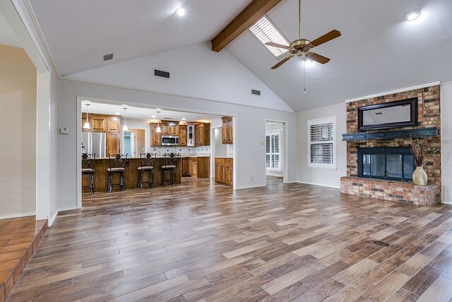 unfurnished living room with ceiling fan, hardwood / wood-style floors, beam ceiling, high vaulted ceiling, and a fireplace