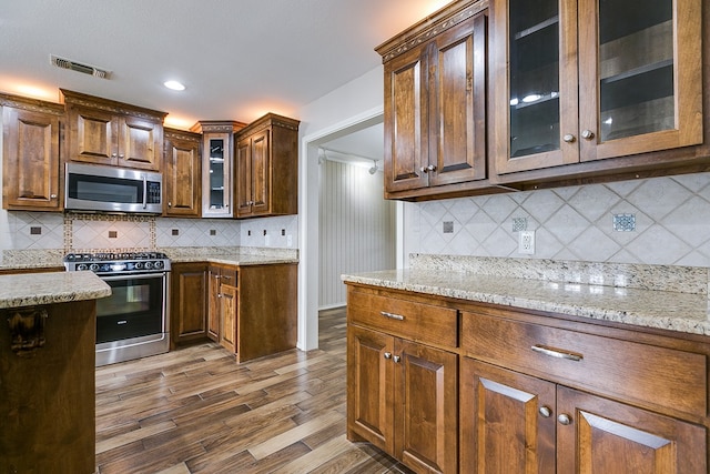 kitchen with stainless steel appliances, hardwood / wood-style floors, backsplash, and light stone counters