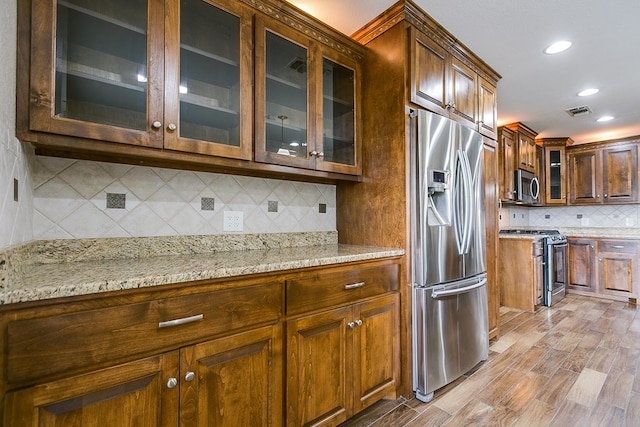 kitchen with light stone counters, backsplash, stainless steel appliances, and light hardwood / wood-style floors