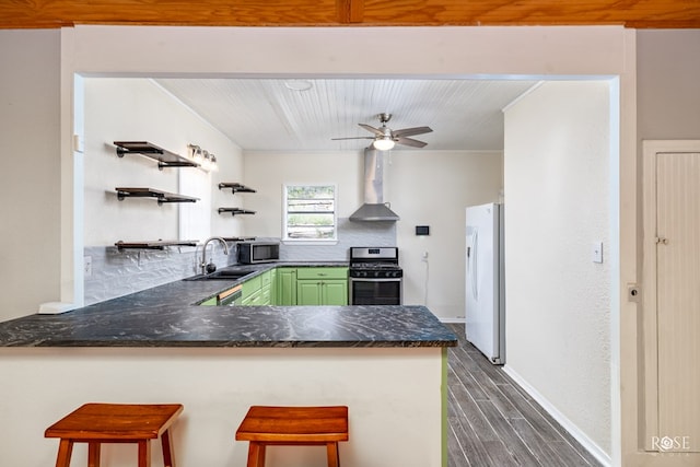 kitchen featuring green cabinetry, a kitchen breakfast bar, kitchen peninsula, stainless steel appliances, and wall chimney range hood