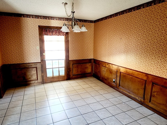 unfurnished dining area featuring an inviting chandelier, a textured ceiling, and light tile patterned floors