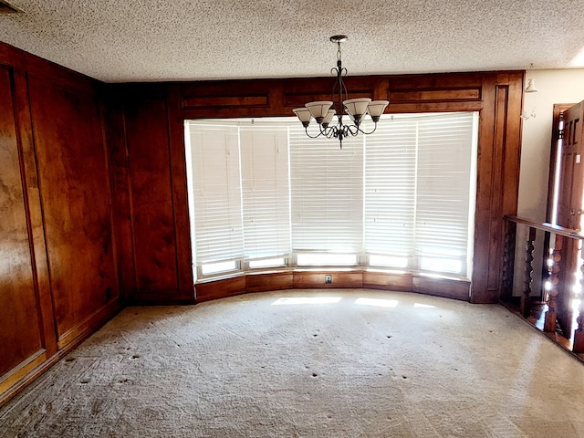 unfurnished dining area with a textured ceiling, light colored carpet, a chandelier, and wood walls