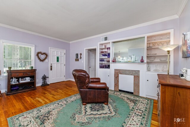 living room featuring hardwood / wood-style flooring, built in features, ornamental molding, and a premium fireplace