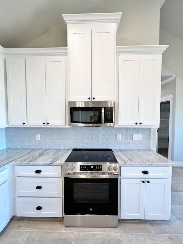 kitchen featuring lofted ceiling, white cabinetry, appliances with stainless steel finishes, light stone countertops, and decorative backsplash