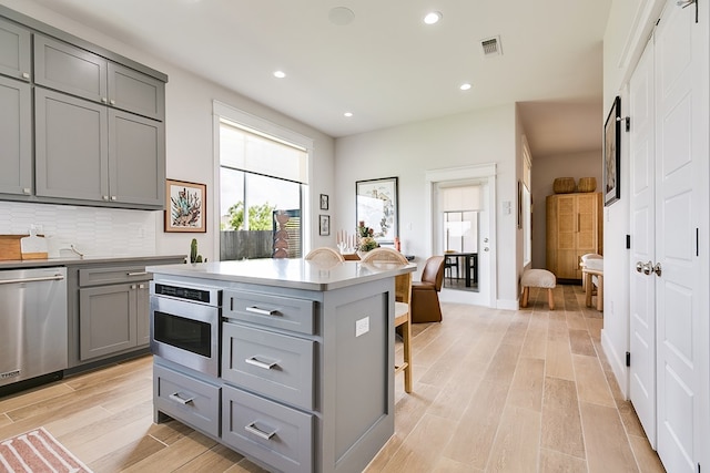 kitchen with stainless steel dishwasher, decorative backsplash, visible vents, light wood finished floors, and gray cabinetry