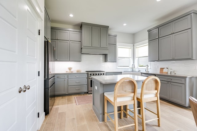 kitchen with a breakfast bar area, gray cabinets, high end range, freestanding refrigerator, and decorative backsplash