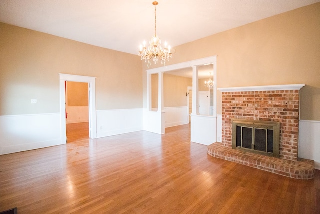 unfurnished living room featuring a chandelier, wood finished floors, a fireplace, and wainscoting