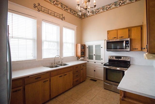 kitchen with an inviting chandelier, light countertops, brown cabinets, stainless steel appliances, and a sink