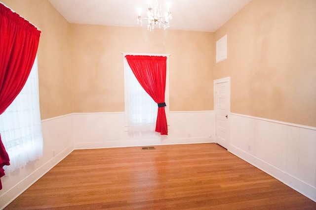 spare room with a chandelier, wood finished floors, visible vents, and a healthy amount of sunlight