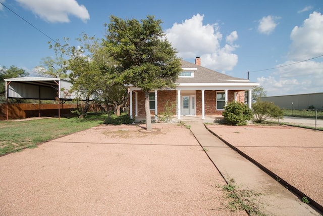 view of front of property with covered porch, a carport, fence, brick siding, and a chimney
