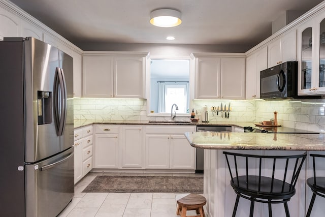 kitchen with white cabinetry, stone countertops, a kitchen breakfast bar, decorative backsplash, and black appliances