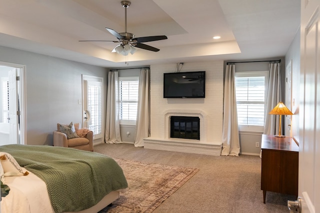 bedroom with ensuite bath, light colored carpet, a large fireplace, a tray ceiling, and ceiling fan