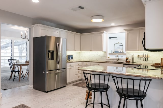 kitchen featuring stainless steel refrigerator with ice dispenser, sink, an inviting chandelier, light stone countertops, and white cabinets