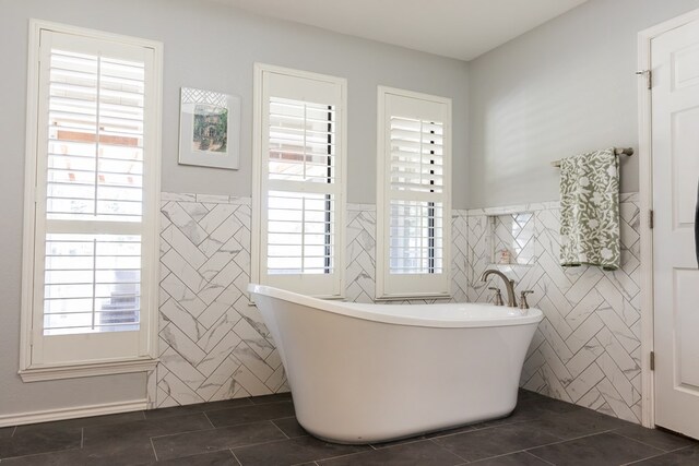 bathroom featuring a wealth of natural light, a washtub, tile patterned floors, and tile walls