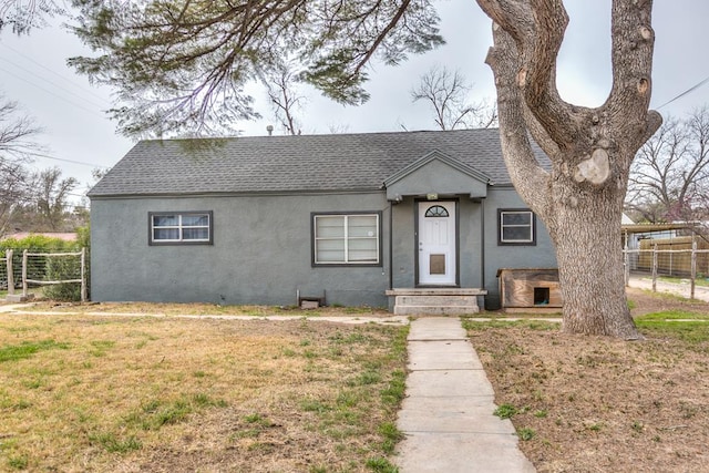 512 Ave J, Ozona, TX 76943 - view of front of house featuring stucco siding, roof with shingles, a front yard, and fence
