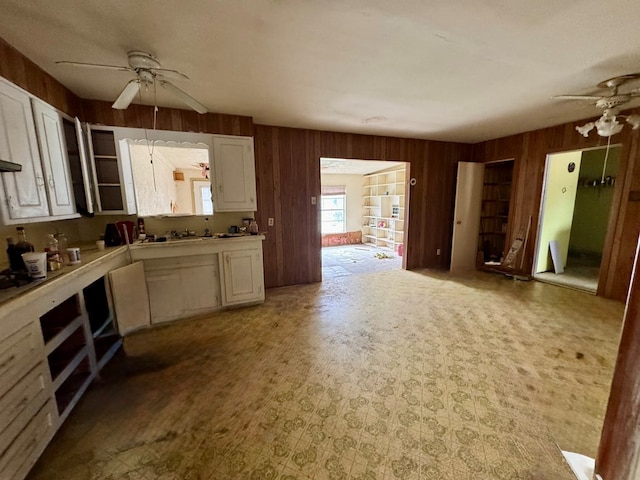 kitchen with wooden walls, a ceiling fan, open floor plan, light countertops, and white cabinetry