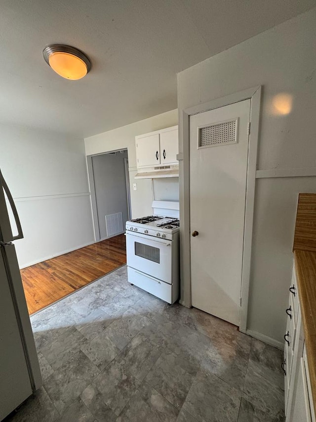 kitchen with white gas range, white cabinets, and stainless steel refrigerator