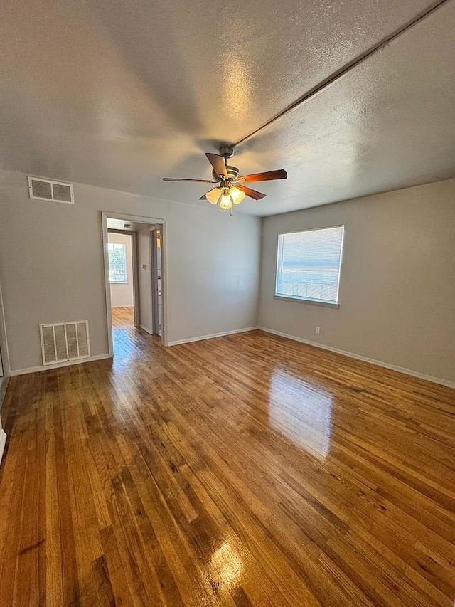 unfurnished room with ceiling fan, hardwood / wood-style flooring, a wealth of natural light, and a textured ceiling