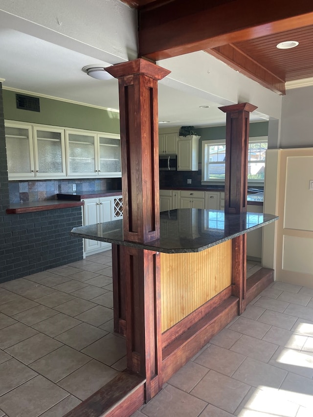 kitchen featuring decorative columns, a kitchen bar, decorative backsplash, light tile patterned floors, and crown molding