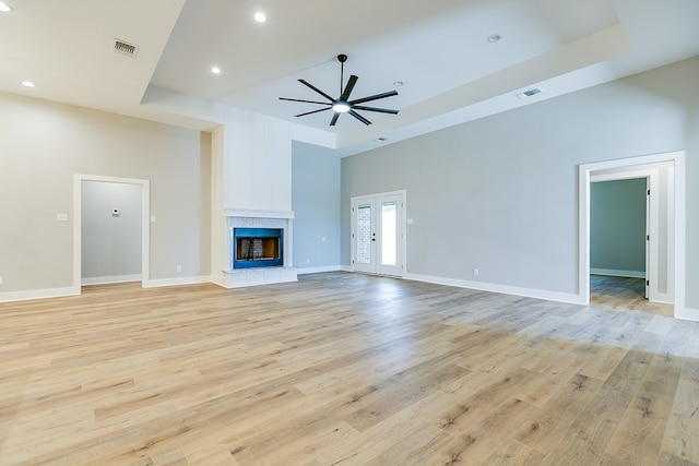 unfurnished living room featuring a towering ceiling, light hardwood / wood-style flooring, a raised ceiling, and ceiling fan