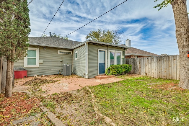 rear view of house with central AC unit and a yard