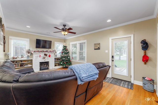 living room with ceiling fan, ornamental molding, a fireplace, and light wood-type flooring