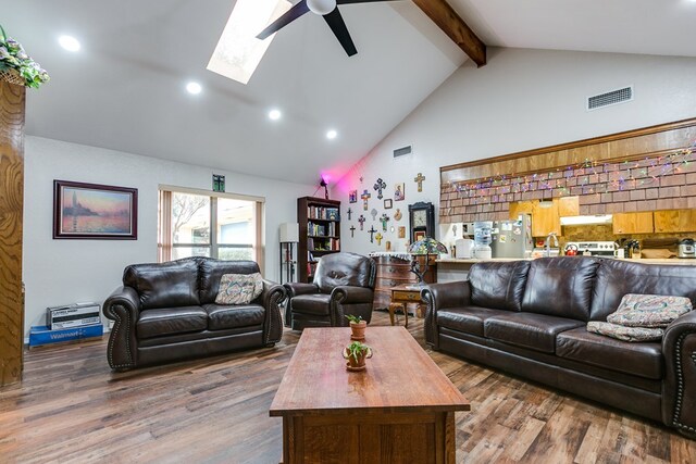 living room featuring hardwood / wood-style flooring, ceiling fan, beam ceiling, a skylight, and high vaulted ceiling