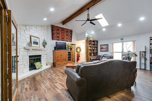 living room with wood-type flooring, a fireplace, vaulted ceiling with skylight, and ceiling fan