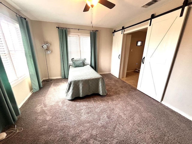 unfurnished bedroom with multiple windows, a barn door, carpet floors, and ceiling fan