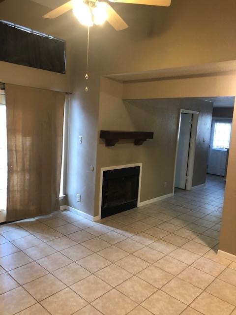 3603 Nevada Dr, San Angelo, TX 76904 - unfurnished living room with ceiling fan, light tile patterned floors, a fireplace, and a towering ceiling