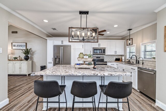 3513 Lindenwood Dr, San Angelo, TX 76904 - kitchen with stainless steel appliances, wood finished floors, a chandelier, white cabinets, and crown molding