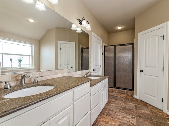 full bath with double vanity, a stall shower, and a sink