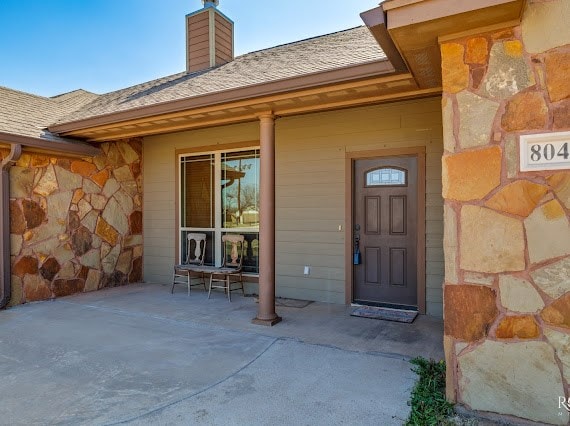 property entrance with a shingled roof, covered porch, and a chimney